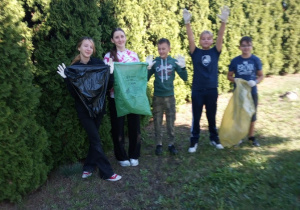 Na zdjęciu grupa uczniów przygotowanych do akcji Sprzątania Świata. Znajdują się w ogrodzie przed szkołą . Uczniowie mają jednorazowe rękawiczki i kolorowe worki do segregacji śmieci.