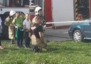 Strażak uczy obsługi wężem strażackim.