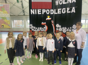 Grupa Krasnale w galowych strojach z wychowawcą na tle ścianki Wolna Niepodległa