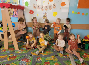 przedszkolaki siedzące na dywanie, trzymające w rękach dynie