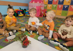 Przedszkolaki siedzące na dywanie z owocami w ręku