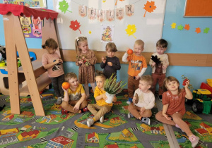 przedszkolaki siedzące na dywanie, trzymają w rękach dynie