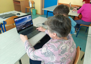 Seniorka wraz z wnukiem uczestniczą w wirtualnej wycieczce odkrywając malownicze szlaki Tatrach Wysokich.