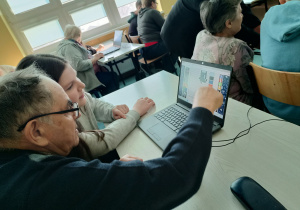 Pradziadek wraz z wnuczką układają na laptopie mozaikę obrazkową.