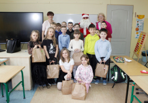 Klasa II a z Mikołajem oraz nauczycielem i przedstawicielem Rady Rodziców. Uczniowie trzymają paczki.