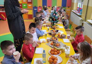 Dzieci siedzą przy wspólnym stole wigilijnym i częstują się smakołykami.