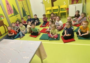 Dzieci siedzące na kolorowych poduszkach podczas spotkania z szalonym naukowcem.