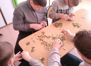 Uczniowie siedzą przy stoliku i przeliczają pieniądze.