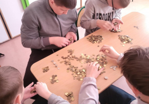 Uczniowie siedzą przy stoliku i przeliczają pieniądze.