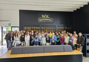 Grupa uczniów na tle szafek z hełmami i napisem "SÓL KŁODAWSKA".