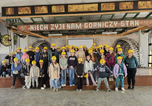 Grupa uczniów z żółtymi hełmami na głowach.