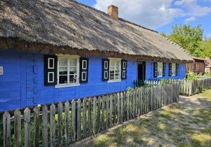 Drewniana, niebieska chata pokryta strzechą.