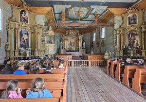 Wnętrze dziewiętnastowiecznego kościoła. Uczniowie siedzą w kościelnych ławkach.