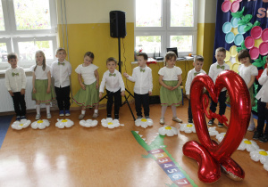 Pół grupy dzieci stoi podczas występów obok balonu foliowego w kształcie serca z napisem love.