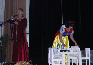 Śnieżka sprząta dom krasnali i narrator stoi przy mikrofonie.