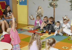 Dzieci z grupy ,,Biedronki” siedzą na dywanie. Uczennice rozmawiają z przedszkolakami na temat przeczytanych wierszy.