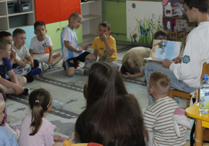 Uczeń z klasy VII b czyta przedszkolakom z grupy ,,Misie” wiersz Aleksandra Fredry ,,Paweł i Gaweł”. Dzieci siedzą na dywanie, a uczeń na krzesełku.