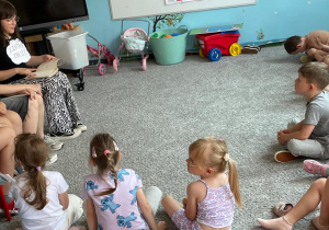 Uczennica klasy VI a zaczyna czytać wiersz Juliana Tuwima ,,Lokomotywa” przedszkolakom z grupy ,,Motylki”. Obok niej siedzą koleżanki, które mają przygotowane wiersze do czytania i nauczyciel bibliotekarz.