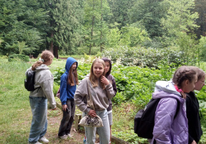 Dzieci idą ścieżkami alpinarium na skalniaku, a u jego podnóża niewielkie oczko wodne.