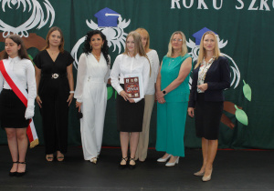 Uczennica klasy 7a z nagrodą, wraz z wychowawcą, panią dyrektor, zastępcą wójta gminy, przewodniczącą Rady Gminy oraz panią inspektor ds. oświaty.