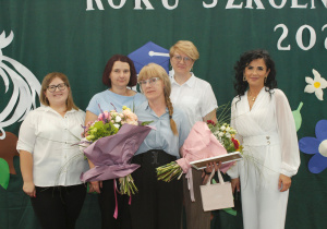 Nauczycielka religii odchodząca na emeryturę, trzymająca kwiaty, z osobami dziękującymi za wieloletnią pracę.