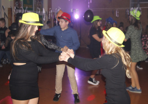 na zdjęciu widnieje tańcząca młodzież z kapeluszami na głowach