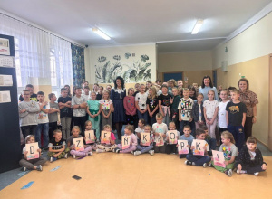 Grupa uczniów z Panią Dyrektor na korytarzu szkolnym. Uczniowie mają ubranie w kropki. Kilku uczniów siedzi na podłodze i trzyma w rękach litery tworzące napis Dzień Kropki.