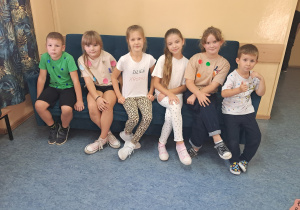 Grupa uczniów siedzi na kanapie. Uczniowie mają ubrania w kropki.