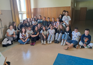 Uczniowie klas 4-7 na szkolnym korytarzu. Mają kolorowe stroje oraz ubrania z papierowymi kółkami.