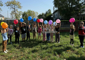 Dzieci z grupy Żabki na trawie podczas zabaw z balonikami.
