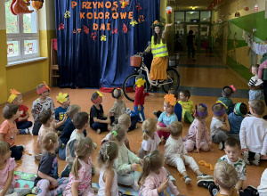 Pani Jesień wjeżdża do oddziału przedszkolnego na rowerze w kasku na głowie i kamizelce odblaskowej machając do dzieci.