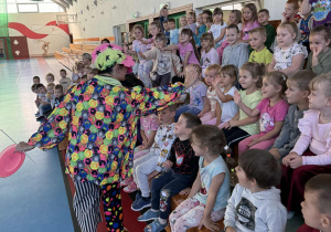 Klaun wita się z dziećmi siedzącymi na widowni.