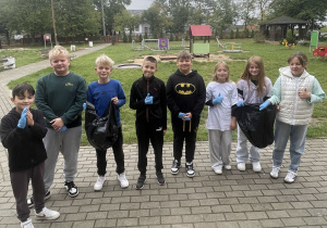 Grupa uczniów przygotowanych do akcji Sprzątania Świata. Znajdują się w ogrodzie przed szkołą