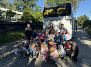 Grupowe zdjęcie dzieci z grupy Żabki i Zuchy na tle autokaru podczas wycieczki do Fabryki Krówek.
