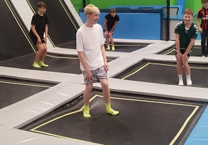 Uczniowie klas 7a oraz 8a w parku trampolin, słuchający instruktora.