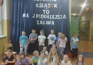 Zdjęcie grupowe dzieci z grupy Zuchy na tle dekoracji "Czytanie książek to najpiękniejsza zabawa".