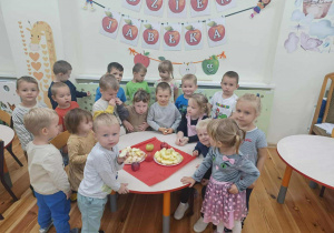 Zajęcie grupowe dzieci z grupy Kamyczki w Dniu Jabłka a na stoliku są pokrojone jabłka do zjedzenia.