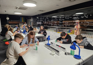 Grupa uczniów siedzi przy stolikach w laboratorium i wykonuje eksperyment.