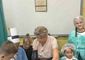 Dzieci w strojach lekarzy i pielęgniarki mierzą ciśnienie Pani Kierownik.