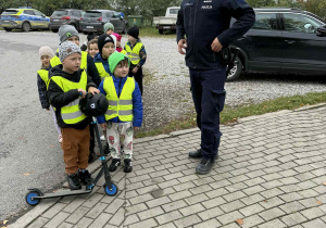 Grupa dzieci z hulajnogą obok stoi policjant.