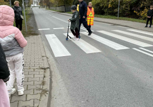 Uczennica przeprowadza hulajnogę po pasach razem z policjantem.