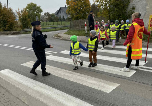 Dzieci z grupy Żabki przechodzą przez przejście dla pieszych pod czujnym okiem policjantów.