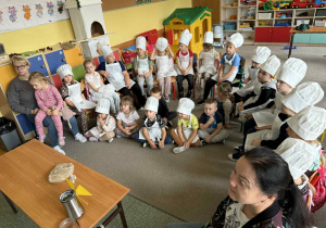 Dzieci z grupy Słoneczka i Żabki siedzą w półkolu w strojach kucharzy.