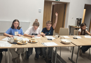 Uczniowie siedzą przy stolikach. Rozwiązują krzyżówki i wykreślanki. Zgłaszają się do odpowiedzi. Pani polonistka sprawdza odpowiedzi dzieci.