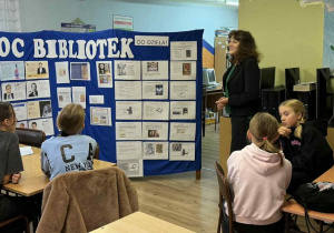 Nauczyciel bibliotekarz z biblioteki szkolnej opowiada uczniom dlaczego sławni ludzie czytają więcej. Na wystawce znajdują się zdjęcia sławnych ludzi, o których opowiada. Przedstawia uczniom również historię pisma i książki.