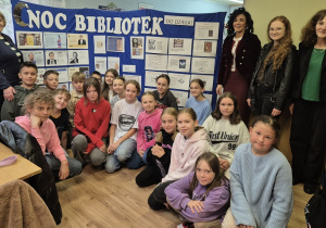 Rozpoczęcie Nocy Bibliotek w Bibliotece Szkoły Podstawowej w Rzeczycy. Pani Dyrektor SP w Rzeczycy, pani Dyrektor GOK w Rzeczycy, pani polonistka i nauczyciel biblioteki szkolnej oraz uczniowie znajdują się na tle tablicy z historią pisma i książki oraz wystawki pt. ,,Dlaczego ludzie sławni czytają więcej?”