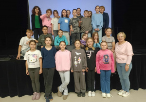 Pamiątkowe zdjęcie na zakończenie Nocy Bibliotek 2025 na terenie GOK w Rzeczycy. Uczniowie i ich opiekunowie stoją na sali widowiskowej GOK w Rzeczycy.