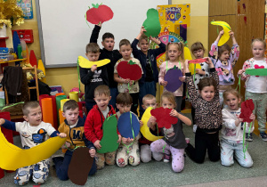 Dzieci z grupy Żabki pozują do grupowego zdjęcia z dużymi owocami i warzywami z papieru.