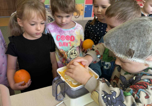 Dzieci wyciskają sok z pomarańczy.