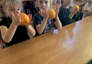 Dziewczynki ćwiczą rączki masując pomarańcze.